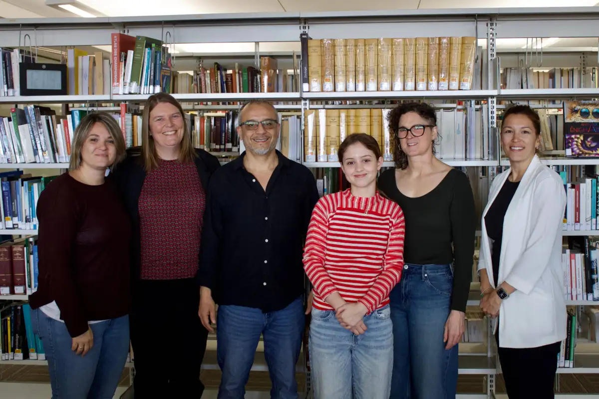 Une étudiante avec des professeur(e)s et membres du personnel devant une bibliothèque de livres.