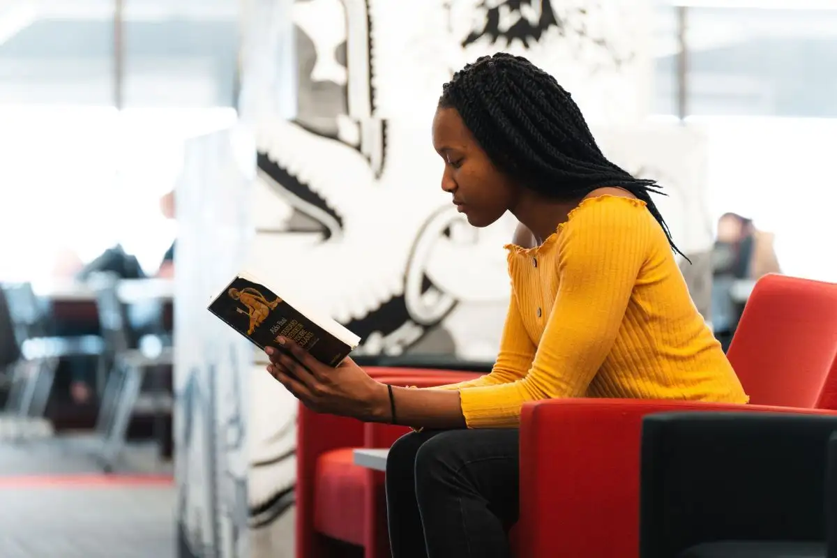 Personne étudiante qui lit un livre assise à la bibliothèque